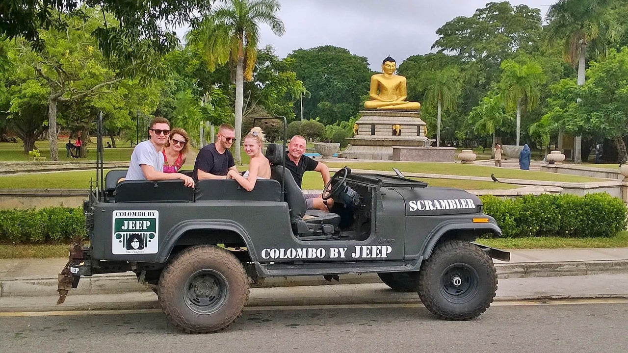 Jeep with passengers in front of a large statue in a park-like setting